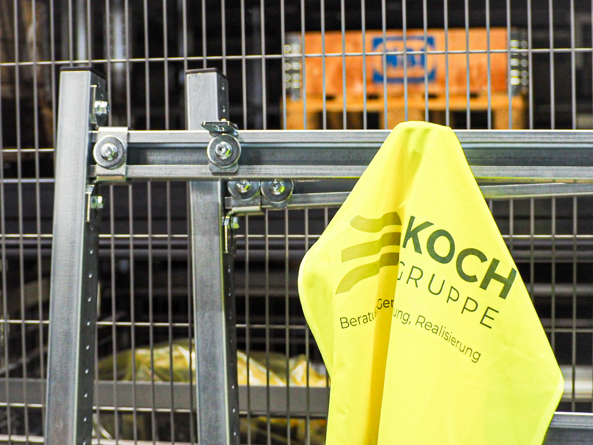 KOCH Gruppe: Symbolbild Realisierung & Inbetriebnahme, Warnweste mit Logo an Gitter